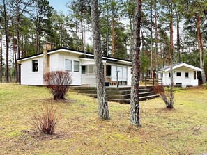 En stuga med en veranda och trappsteg som leder upp till entrén, omgiven av träd.