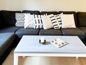 Un salon moderne avec un canapé gris, des coussins blancs, une table basse blanche et une bougie.