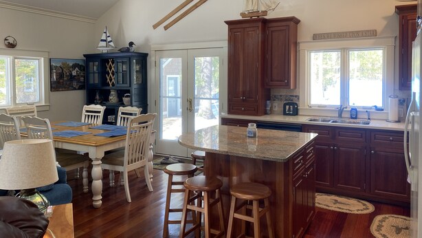 A spacious kitchen with wooden cabinets, a large island, and a dining area with chairs and a table. - Torch Lake Cabin near launch with boat option (Rapid City)