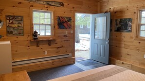 A cozy cabin room with wooden walls, a bed, a heater, a window, and a door. - Torch Lake Cabin near launch with boat option (Rapid City)