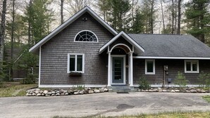 A two-story house with a grey shingle exterior, a front porch, and a stone foundation. - Torch Lake Cabin near launch with boat option (Rapid City)