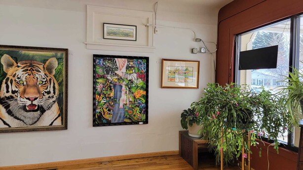 Una habitación con suelo de madera, un cuadro grande de un tigre, un cuadro abstracto colorido y una planta en maceta junto a una ventana.