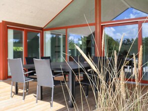 Un área de estar al aire libre con mesas y sillas, ventanas amplias y vista al cielo.