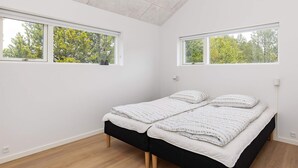 Un dormitorio con una cama, dos ventanas y vistas a árboles.