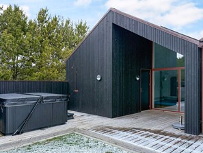 Un bâtiment moderne doté d’une grande porte vitrée et d’un jacuzzi installé sur une terrasse en bois.