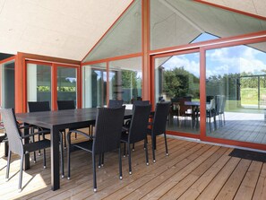 Un área de comedor al aire libre con terraza de madera, paredes de vidrio y vista despejada del paisaje circundante.