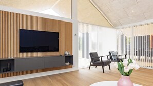 Una sala de estar moderna con un televisor de pantalla plana montado en una pared de paneles de madera, una mesa de centro redonda blanca y un jarrón rosa con flores.