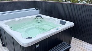 Un jacuzzi con asiento integrado y panel de control, sobre una terraza de madera sobre un fondo oscuro.