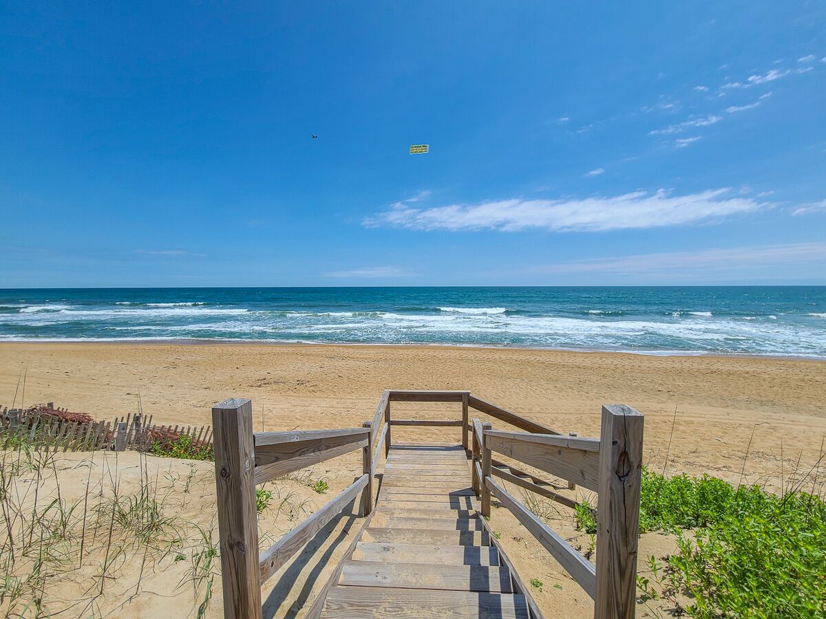 Une promenade en bois qui mène à une plage où l’on peut voir des vagues et un ciel dégagé.