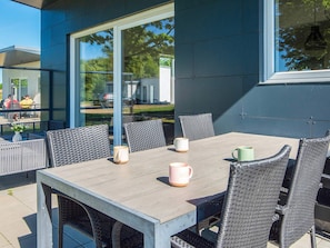 An outdoor dining area with a table and chairs, large windows, and a view of the surrounding area. - 4 Star Holiday Home in Ringkobing (Ringkobing)