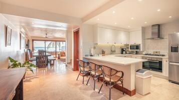 A modern kitchen with white cabinets, a central island with bar stools, a built-in oven, and a stainless steel refrigerator.