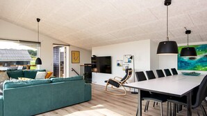 A modern living room with a teal sofa, a dining table with black chairs, and a large abstract painting on the wall. - 10 Person Holiday Home in Bjert (Bjert)