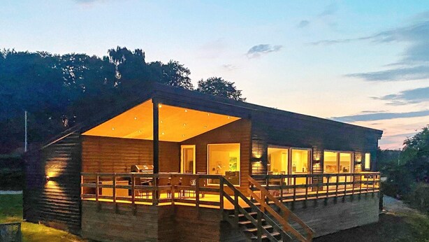 A modern house with a large glass front, wooden deck, and a staircase leading to the entrance. - 10 Person Holiday Home in Bjert (Bjert)