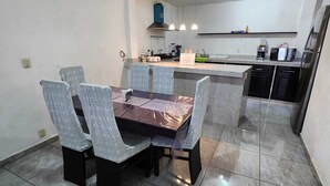 A modern kitchen with a central island, a dining area with patterned chairs, and a tiled floor.