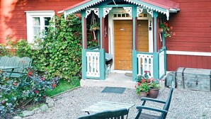Ein traditionelles Holzhaus mit Veranda, einer Tür und einem kleinen Garten mit Pflanzen und einer Bank.