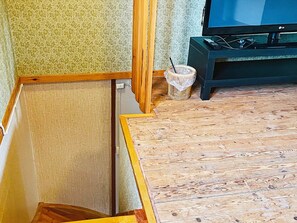 Een kamer met een televisie op een standaard, een gevlochten mand en een gedeeltelijk zichtbare houten vloer.