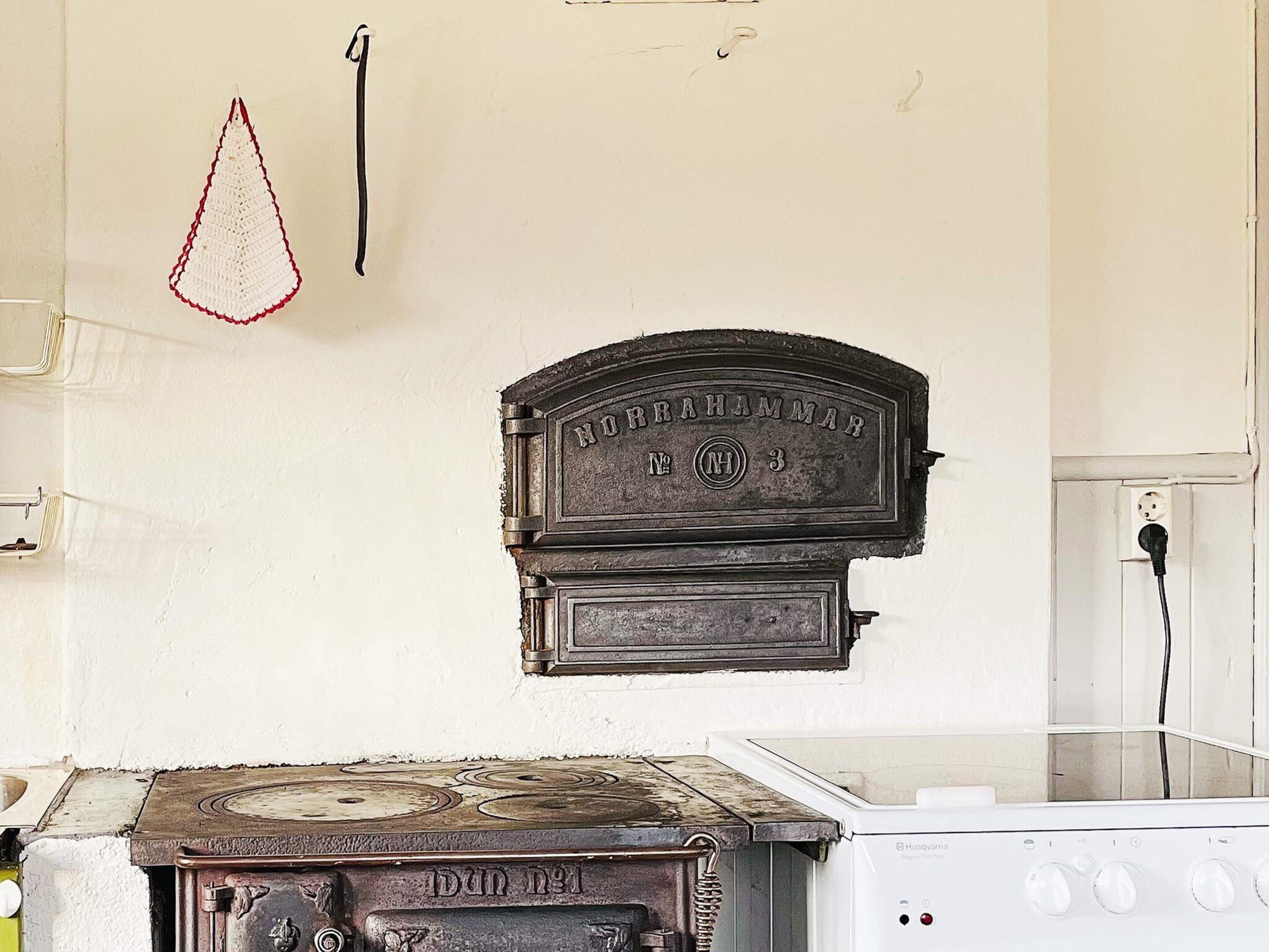 A kitchen with a vintage stove, a hanging kitchen towel, and a wall-mounted electrical outlet.