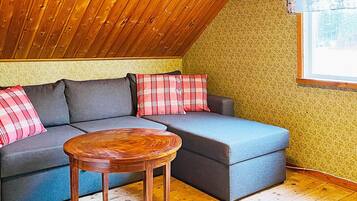 Ein gemütliches Zimmer mit schrägem Dach, einem Ecksofa mit Karokissen und einem Holztisch.