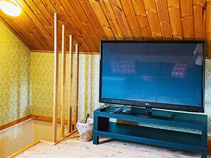 A room with a large flat-screen TV on a stand, wooden ceiling, and patterned wallpaper. - 5 Person Holiday Home in Fargelanda (Färgelanda)