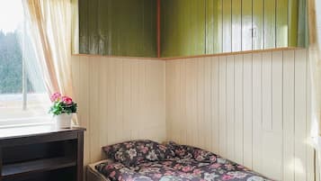 A small room with a single bed, a window with curtains, and a shelf with a potted plant.