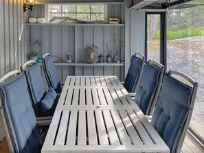 A dining area with a white table and chairs, a window with a view of trees, and shelves with decorative items. - 10 Person Holiday Home in Halden (Halden)