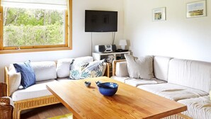 Een woonkamer met een bank, een houten salontafel, een televisie en een raam met uitzicht op groen.