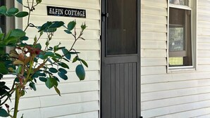 A white building with a dark gray door, a sign reading "ELFIN COTTAGE", and a window with a screen. - A charming cottage with picturesque rural views over surrounding rural farm land (Melville Forest)