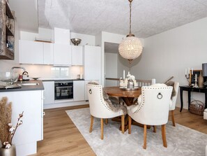 A modern kitchen with white cabinets, a wooden dining table with chairs, and a chandelier.