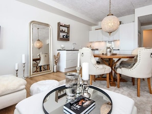 Uma sala de estar moderna com uma mesa de centro de vidro, móveis brancos e um candelabro.