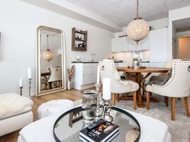 Uma sala de estar moderna com uma mesa de centro de vidro, móveis brancos e um candelabro.