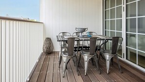 Een balkon met een tafel, stoelen, een groot raam en een decoratieve vaas.