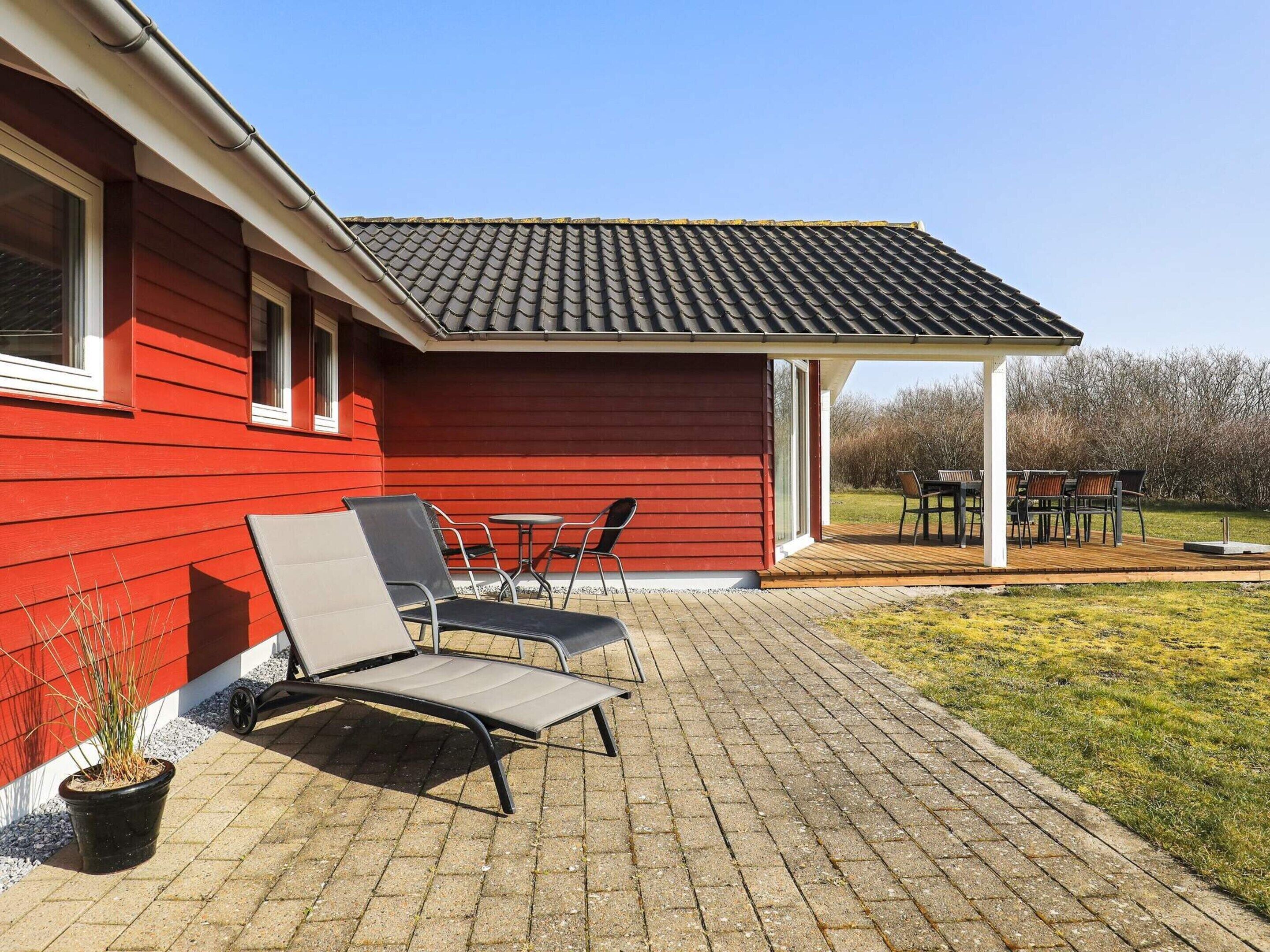 A red building with a covered patio area featuring outdoor seating and a potted plant.