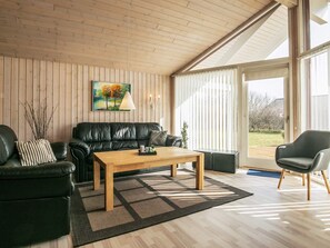 A living room with a wooden ceiling, a black leather sofa, a wooden coffee table, and a view through a glass door.