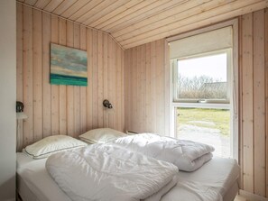 A bedroom with a wooden ceiling, a bed with white bedding, a painting on the wall, and a window with a view of the outdoors.