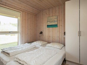 A bedroom with two beds, a window, a painting, and a wardrobe.