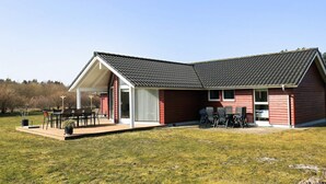 A red building with a sloped roof and a covered patio area with outdoor furniture. - 8 Person Holiday Home in Brovst (Brovst)