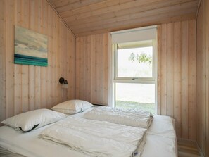 A room with wooden walls, a bed with white bedding, a painting, and a window with a view. - 8 Person Holiday Home in Brovst (Brovst)