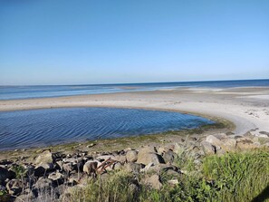 Ein Strand mit klarem, blauem Wasser, einem sandigen Ufer und großen Felsen im Vordergrund.