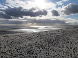 A beach with footprints leading to the water, a wide sandy area, and a cloudy sky.