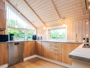A modern kitchen with wooden cabinets, stainless steel appliances, and large windows providing natural light.