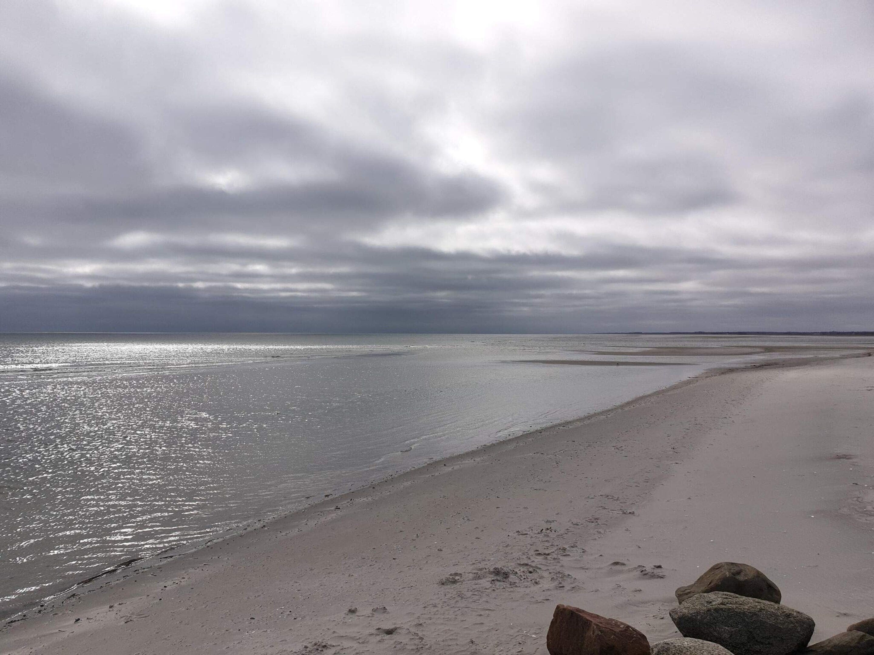 Una spiaggia con un mare calmo, un cielo nuvoloso e una riva sabbiosa con rocce.