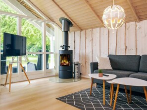 A modern living room with a wood-burning stove, a television on a tripod stand, and a grey sofa. - 4 Star Holiday Home in Asaa (Asaa)