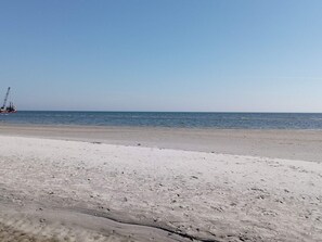 A beach with a clear sky, a sandy shore, and a distant offshore structure.