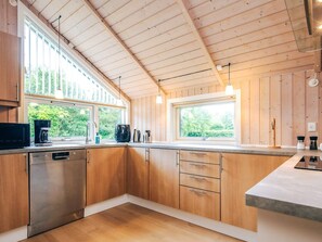 A modern kitchen with wooden cabinets, stainless steel appliances, and large windows providing natural light. - 4 Star Holiday Home in Asaa (Asaa)