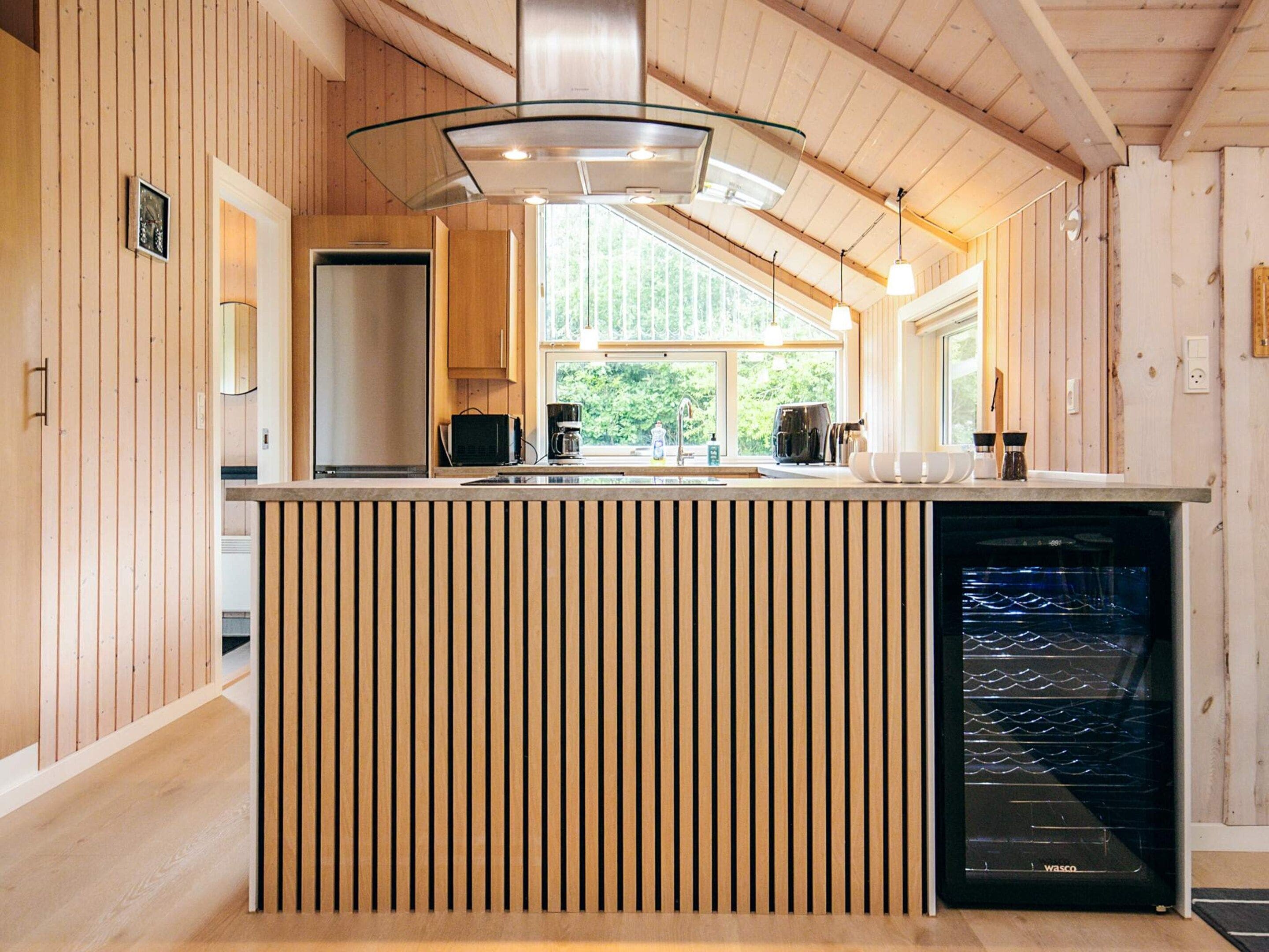 A modern kitchen with wooden paneling, a built-in dishwasher, and a large window providing natural light.