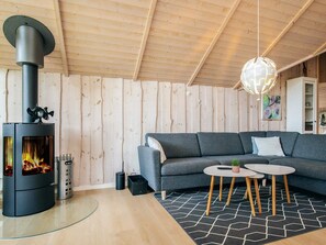 A modern living room with a wood-burning stove, a grey sofa, a round coffee table, and a hanging light fixture.