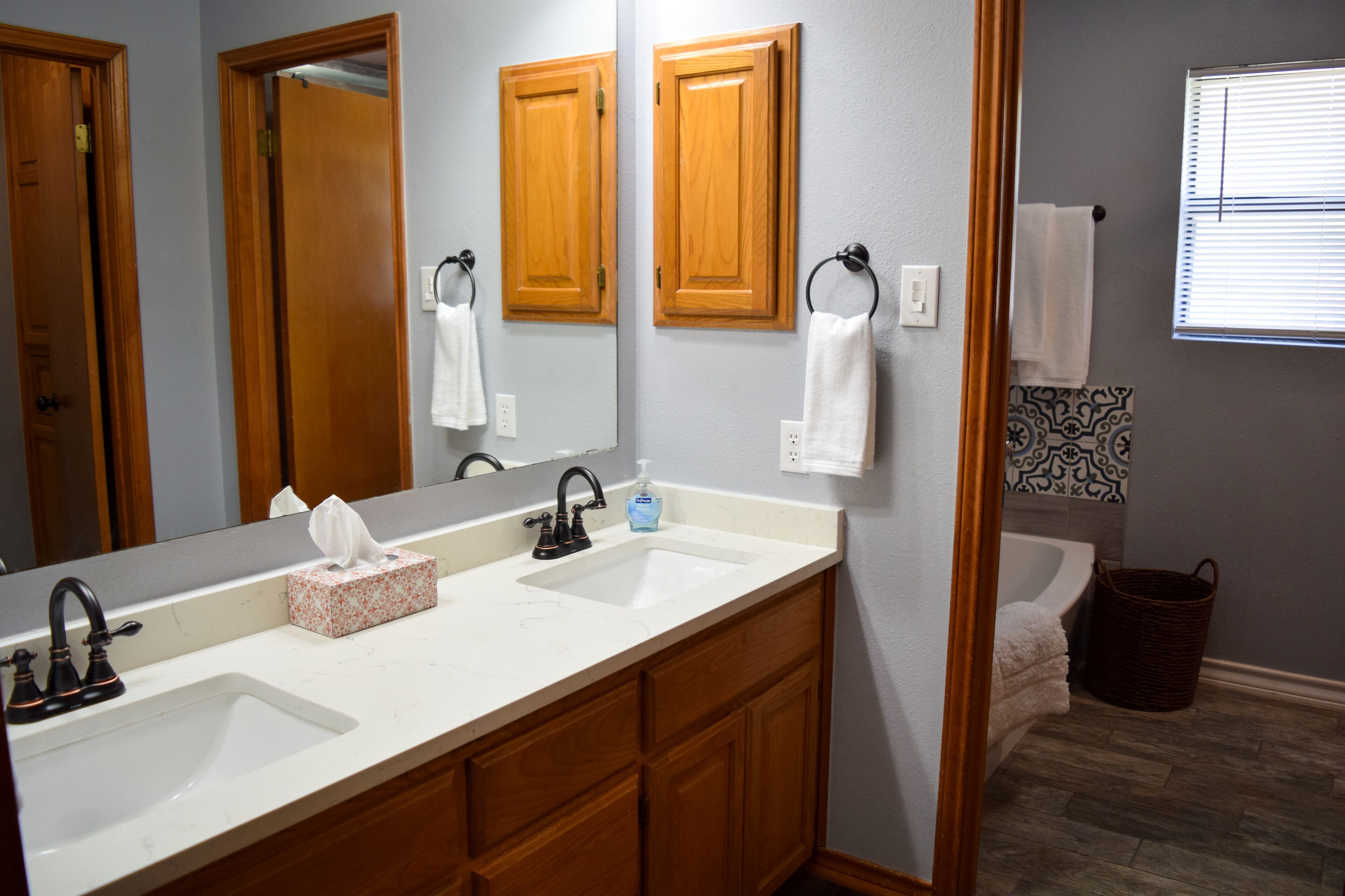 A bathroom with two sinks, wooden cabinets, a large mirror, and a window with blinds.