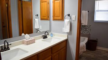 A bathroom with two sinks, wooden cabinets, a large mirror, and a window with blinds.