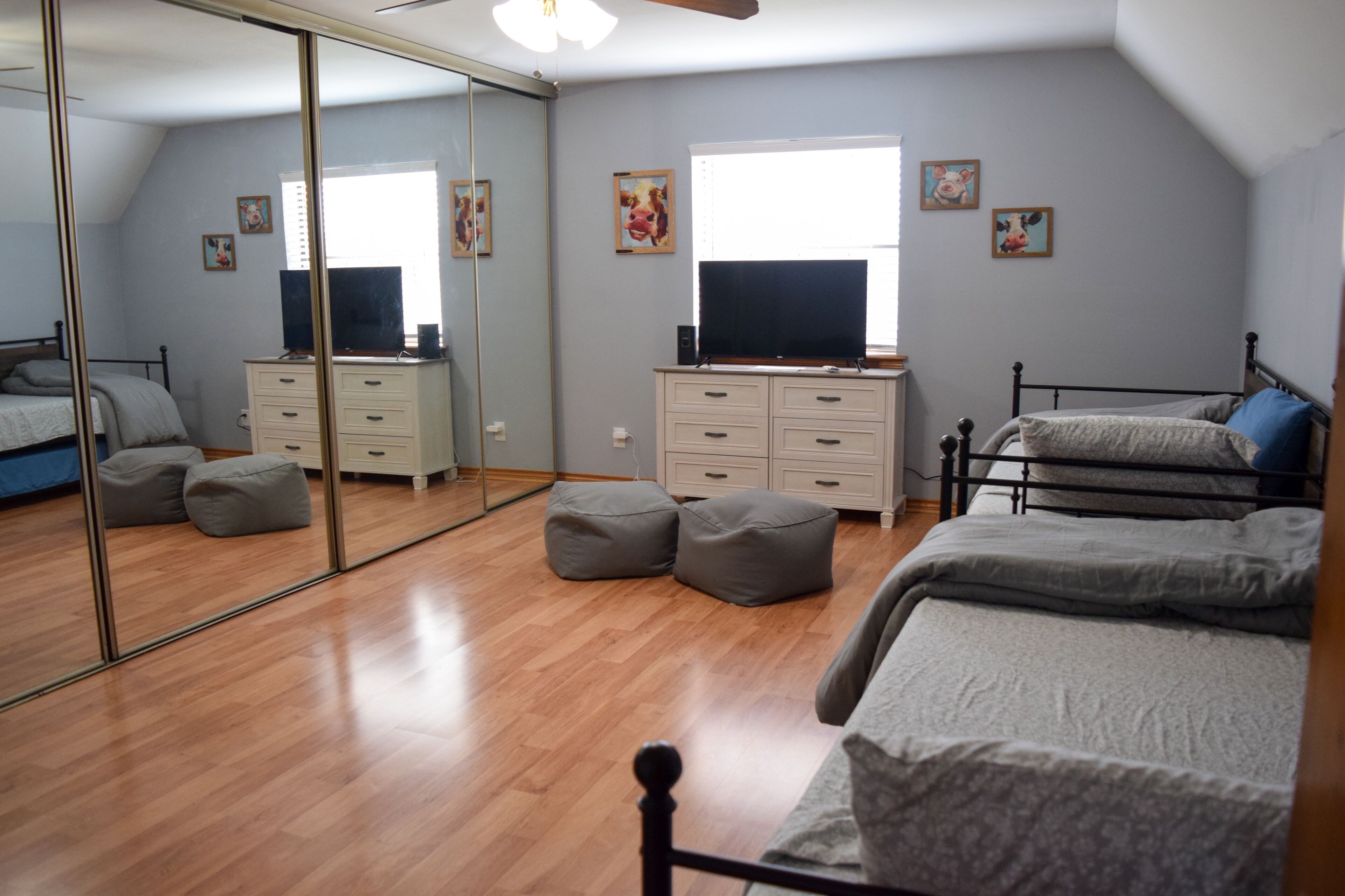 A bedroom with a large mirror, a bed with grey bedding, a dresser, and a television.