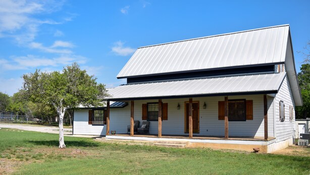 Une maison de plain-pied avec un toit en métal à pente, une véranda dotée de piliers en bois et un petit jardin.